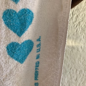 Puede incluir: Toalla blanca con un patr&oacute;n de coraz&oacute;n azul. El texto "Showers Printed in U.S.A." est&aacute; impreso en la toalla.