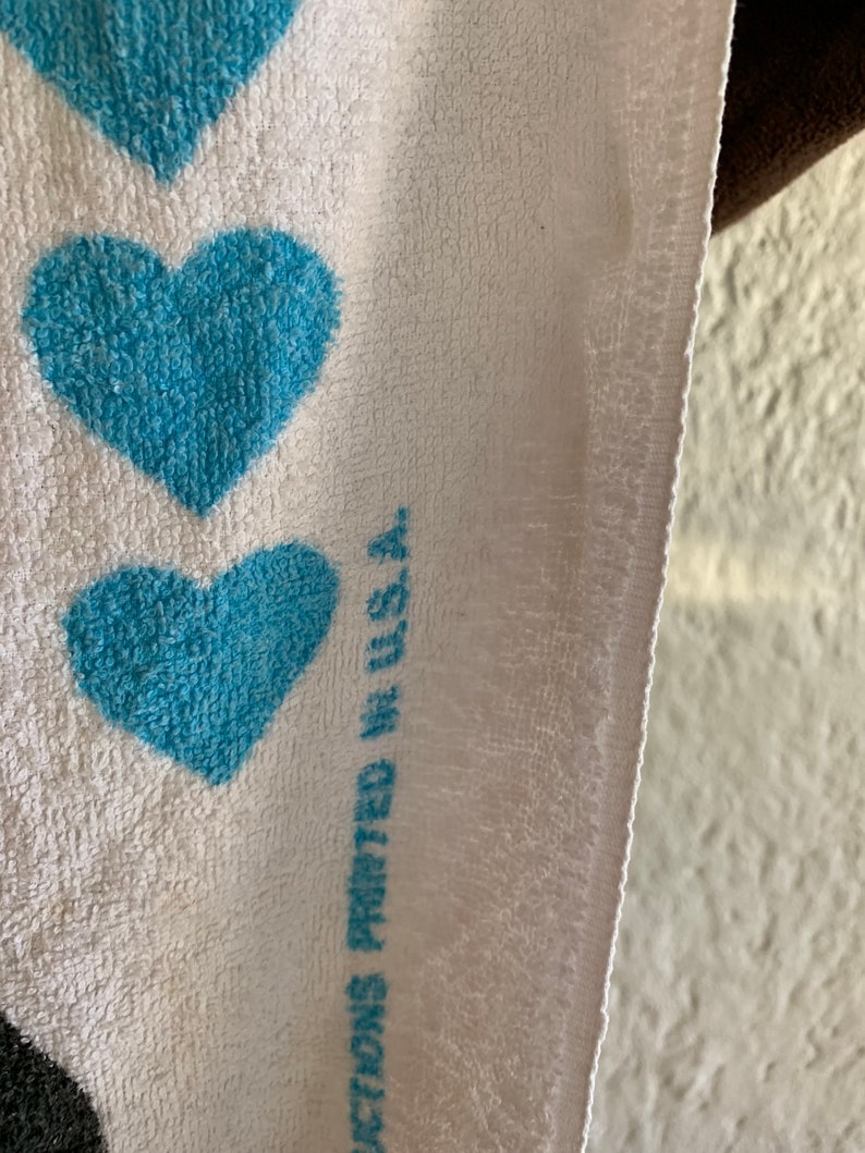 Puede incluir: Toalla blanca con un patr&oacute;n de coraz&oacute;n azul. El texto "Showers Printed in U.S.A." est&aacute; impreso en la toalla.