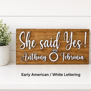 May include: A rectangular wooden sign with a medium brown finish featuring white raised lettering that reads She said Yes! Anthony and Febronia with a white diamond ring icon centered between the names. The text Early American / White Lettering is below.