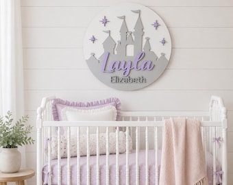 May include: A circular wall sign featuring a gray castle silhouette on a white background with purple star accents. The name Layla is written in a purple script font, with the name Elizabeth printed in a smaller gray sans-serif font below it.