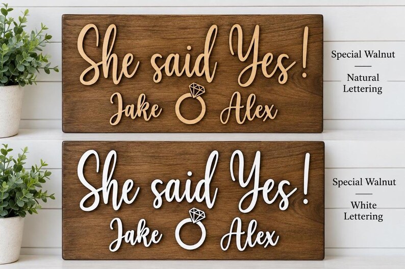 May include: Two rectangular dark walnut wood signs featuring the text She said Yes! with the names Jake and Alex and a diamond ring icon. The top sign has natural wood lettering, while the bottom sign features white lettering on the wood surface.