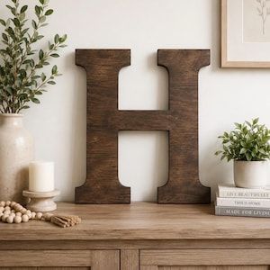 May include: A large, dark brown wooden letter H with a visible wood grain texture. The letter features a block-style serif font with straight vertical sides and a horizontal crossbar. The surface has a smooth, matte finish throughout the piece.