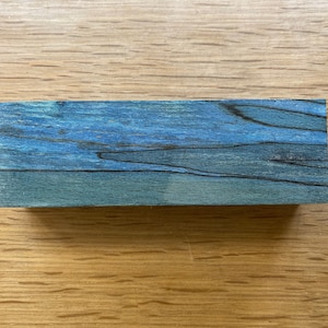 May include: A close-up of a blue and black wood block. The wood has a natural grain pattern and is a dark blue colour with black streaks.
