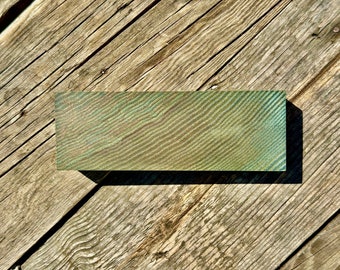 May include: A close-up of a green wood block with a wood grain pattern. The block is sitting on a wooden surface.