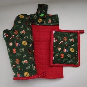 May include: A set of three green and red Christmas themed kitchen accessories. The set includes a potholder, an oven mitt, and a tea towel. The accessories feature a repeating pattern of Star Wars characters and Christmas symbols.