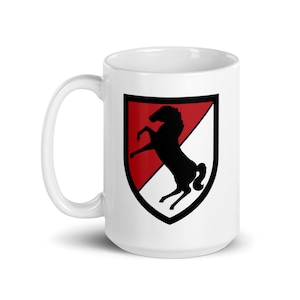 May include: White ceramic mug with a red and white shield featuring a black silhouette of a rearing horse. The shield has a black outline.