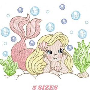 May include: An embroidered design of a mermaid with blonde hair and a pink tail, resting on a sandy surface. Bubbles and seaweed surround the mermaid. The text "5 SIZES" is below the image.