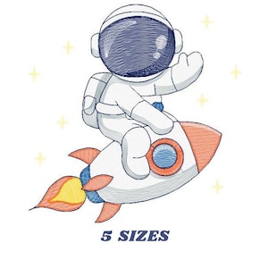 Puede incluir: Un diseño bordado de un astronauta de dibujos animados con un traje espacial blanco montando un cohete con llamas naranjas. El diseño está rodeado de pequeñas estrellas amarillas.