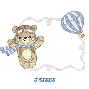 May include: Embroidered design of a brown bear wearing a pilot's hat and scarf, flying in a hot air balloon with blue and white stripes. The design is surrounded by a white cloud-like frame. The text "5 SIZES" is below the design.