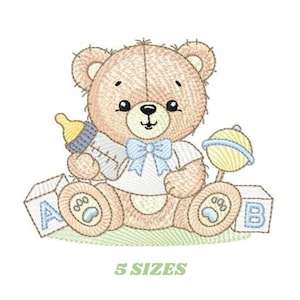 Puede incluir: Diseño bordado de un oso de peluche marrón que sostiene un biberón y un sonajero. El oso está sentado en un parche de hierba verde con dos bloques que dicen "A" y "B".