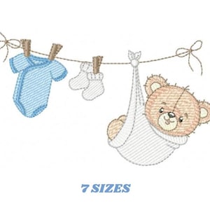 Puede incluir: Diseño bordado con ropa de bebé y un osito de peluche colgados de un tendedero. El diseño incluye un body azul, calcetines blancos y un osito de peluche en un portabebés blanco. El texto "7 SIZES" está debajo.