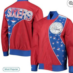 May include: A red Philadelphia 76ers full-snap warmup jacket featuring blue accents, a large Sixers logo on the back, and a circular team graphic on the front chest. The design includes a blue panel decorated with white and red stars on the front.