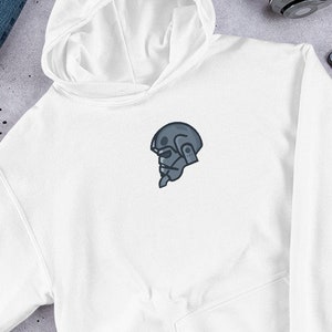 Puede incluir: Sudadera con capucha blanca con una peque&ntilde;a figura de robot gris con casco en la parte delantera.
