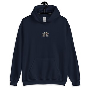May include: A navy blue hoodie featuring a small embroidered image of two cartoon characters wearing helmets and holding weapons. The characters are standing side-by-side and appear to be in a playful pose.