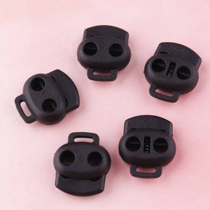 May include: Five black plastic toggle clasps with two holes each. The clasps have a small loop on the side for attaching to a cord or strap.