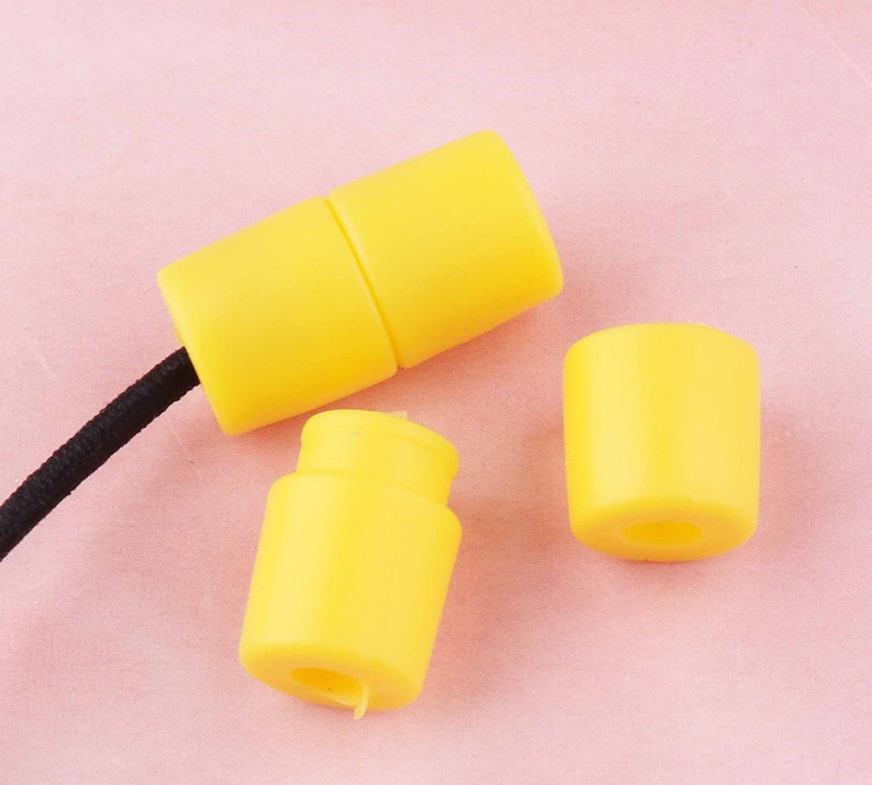 May include: Three yellow plastic cord end stoppers. Two of the stoppers are connected to a black cord.
