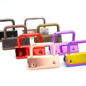 May include: A set of eight metal D-ring clasps in various colors, including black, brown, red, rose gold, purple, and iridescent. The clasps are all the same size and shape, with a rectangular base and a D-shaped ring.