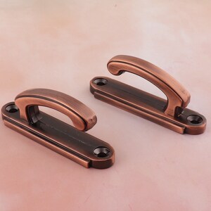 May include: Two antique copper-toned hooks with a simple design. Each hook has a rounded top and a flat base with a screw hole.