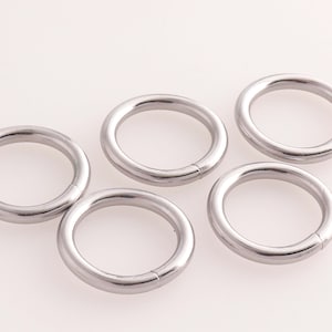 Puede incluir: Cinco anillos de metal plateado, cada uno con forma circular y un acabado liso y pulido.