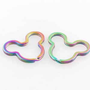 Puede incluir: Dos llaveros de metal con forma de cabeza de Mickey Mouse, de color arcoíris.