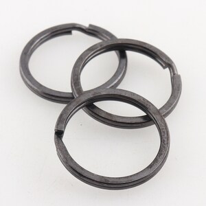 May include: Three black metal key rings, each with a different diameter, are stacked on top of each other.