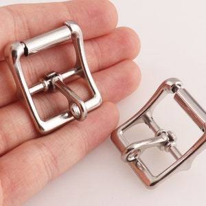 May include: Two silver metal belt buckles with a rectangular shape and a sliding buckle closure.