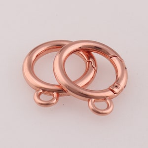 May include: Two rose gold metal swivel clasps with a small loop on each. The clasps are open and ready to be attached to a chain or other jewellery.