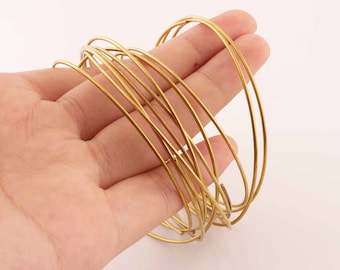 Pode incluir: Um conjunto de 15 anéis de arame metálico dourado, empilhados e segurados em uma mão. Os anéis são finos e delicados, perfeitos para a criação de joias ou outros projetos.