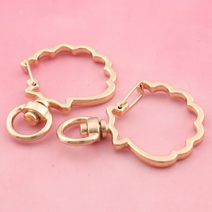 May include: Two gold-toned metal keychains with a scalloped design. One keychain has a round ring, while the other has a smaller ring with a swivel clasp.