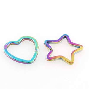 Puede incluir: Dos llaveros de metal, uno con forma de corazón y el otro con forma de estrella. Ambos son iridiscentes con colores arcoíris.