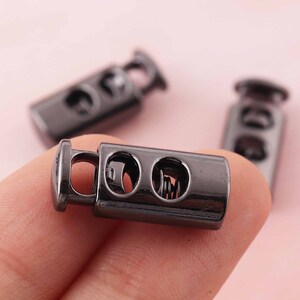 Puede incluir: Tres topes de cordón de metal negro con un mecanismo de resorte. Los topes están diseñados para ser utilizados en cordones o cordones de ajuste.