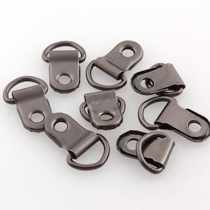 Puede incluir: Un grupo de ocho piezas de herrajes de anillo en D de metal en acabado bronce oscuro. Los anillos en D están diseñados para sujetarse a tela o cuero.