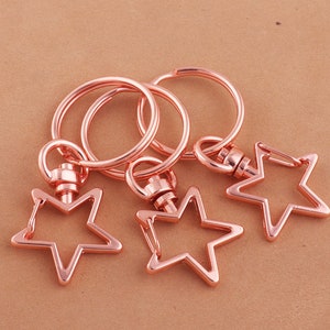May include: Three rose gold keyrings with star-shaped charms. Each keyring has a circular ring and a swivel clasp.