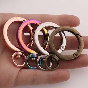 May include: A set of five metal key rings in various colors, including silver, gold, and rainbow. The key rings are all different sizes and have a variety of shapes, including round, oval, and square.