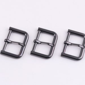 May include: Three black metal belt buckles. The buckles are rectangular with rounded corners and have a smooth, polished finish.