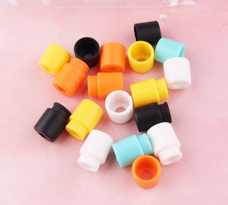 May include: Assortment of colorful plastic end caps in various colors, including black, white, yellow, orange, and blue. The end caps are small and round, with a hole in the center.