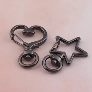 Puede incluir: Dos llaveros de metal negro, uno con forma de corazón y el otro con forma de estrella. Ambos llaveros tienen un cierre giratorio y un anillo.