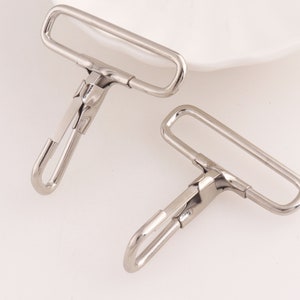 May include: Two silver metal swivel hooks with a rectangular loop on one end and a hook on the other end.