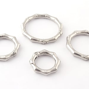 Puede incluir: Tres llaveros de metal plateado con un diseño de bambú. Los anillos están abiertos y tienen un cierre de resorte.