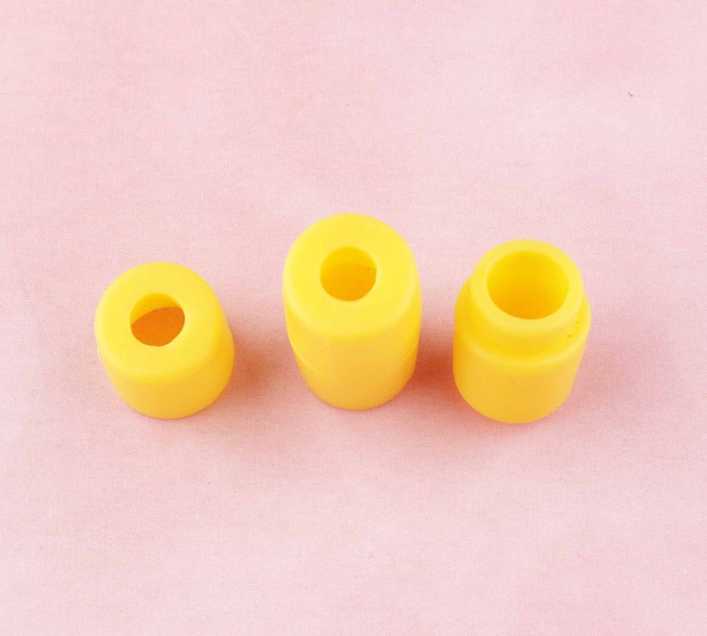May include: Three yellow rubber stoppers of different sizes. The stoppers are round with a hole in the center.
