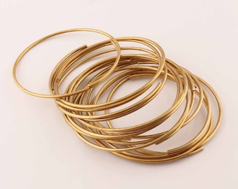 Pode incluir: Um conjunto de 15 argolas de metal douradas, empilhadas e sobrepostas. As argolas são todas do mesmo tamanho e são feitas de um fio fino e redondo.