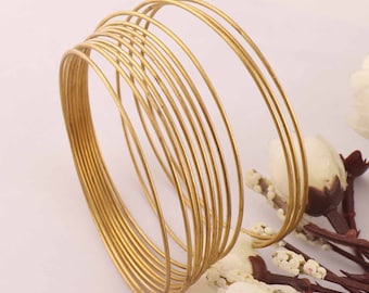 Pode incluir: Um conjunto de 15 pulseiras de metal dourado empilhadas. As pulseiras são finas e têm um acabamento liso e polido.