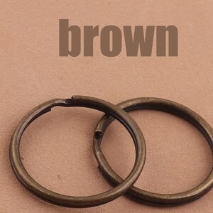Peut inclure: Deux anneaux de clés en métal brun, l'un légèrement plus grand que l'autre, sur un fond brun clair. Le mot "brown" est imprimé en lettres noires au-dessus des anneaux de clés.