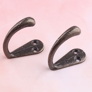 Peut inclure: Deux crochets en métal de style antique avec une finition bronze foncé. Chaque crochet a une forme incurvée et deux trous pour le montage.