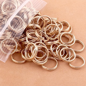 May include: A large quantity of gold-colored metal key rings in a clear plastic bag. The key rings are spilling out of the bag onto a brown surface.
