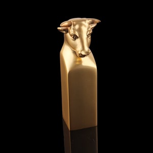May include: A gold-coloured bull's head sculpture on a rectangular base. The sculpture is made of metal and has a realistic appearance.