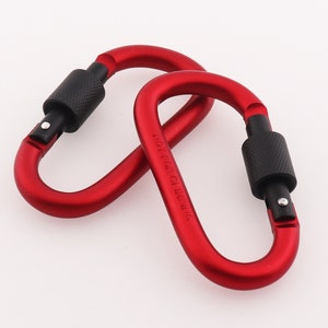Peut inclure: Deux mousquetons en métal rouge avec des poignées noires. Les mousquetons sont étiquetés "NOT FOR CLIMBING".