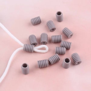 Pode incluir: Um close-up de um grupo de tampas de cordão de silicone cinza. As tampas são projetadas para evitar que os cordões se desgastem e são perfeitas para uso com cordões de fones de ouvido, cabos de carregamento e outros tipos de cordões.