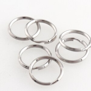 May include: Six silver key rings, all the same size, are stacked on top of each other. The rings are made of metal and have a smooth, shiny finish.