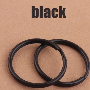 Könnte beinhalten: Zwei schwarze Schlüsselringe aus Metall, ineinander verschlungen, auf braunem Hintergrund. Das Wort "schwarz" ist in schwarzer Schrift über den Schlüsselringen geschrieben.